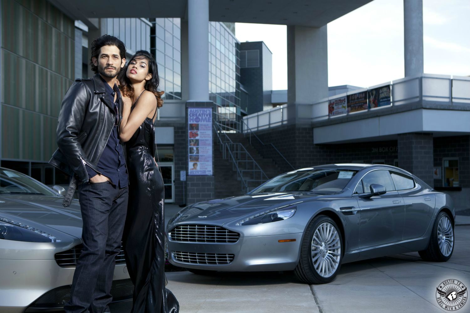 hispanic male and female fashion models wearing leather and vinyl high fashion clothes  in front of two aston martins in front of the long center for the performing arts